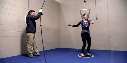 Der Coach zieht Mirai an der harness hoch, damit sie die Rotation und Landung trainieren kann.