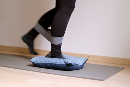 While one leg is on the cushion, the other is moved in a semi-circle from front to back against the resistance of the fitness band.