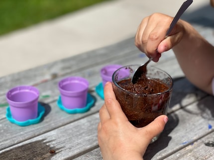 First the three-year-old spooned the wet soil into the pots.