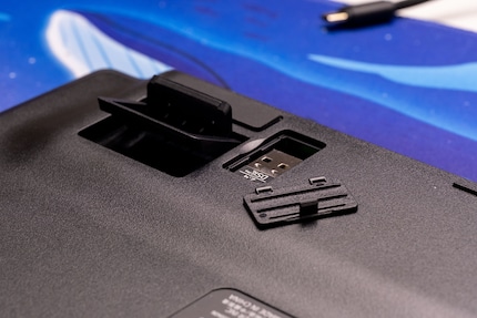 Der Deckel der Dongle-Garage lässt sich nur schwer öffnen und wirkt billig. Die Klappfüsse daneben, mit denen sich der Tippwinkel der Deathstalker V2 Pro TKL verstellen lässt, sind hingen gut.