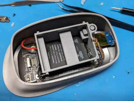 Die Unterseite der zweigeteilten Maus klebt mittels doppelseitigem Klebeband im Gehäuse. Auf dem Akku befindet sich ein Abstandshalter aus dem 3D-Drucker.