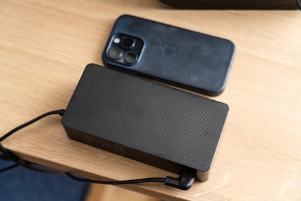 Externe Netzteile ermöglichen leichtere Geräte. Dafür muss ich auf dem Tisch einen Platz für sie finden. Zum Vergleich daneben ein iPhone 15 Pro.