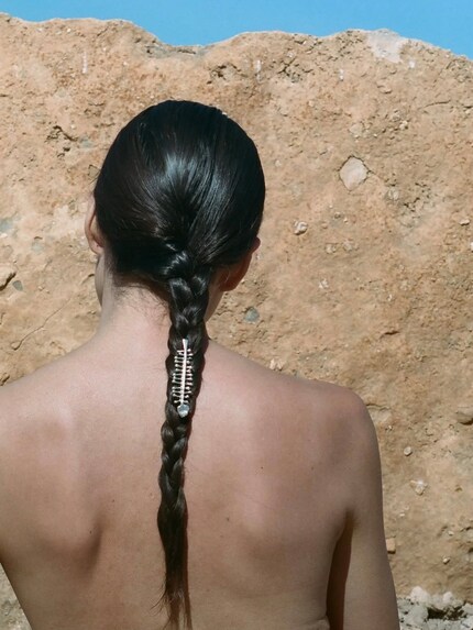 Das Schmucklabel Alighieri platziert eine Brosche im geflochtenen Haar.
