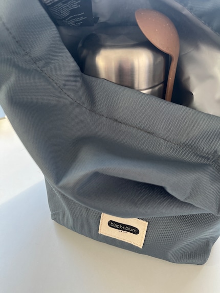 Die Tasche hat einen Rolltop-Verschluss und ist innen isoliert, um kühl zu halten.
