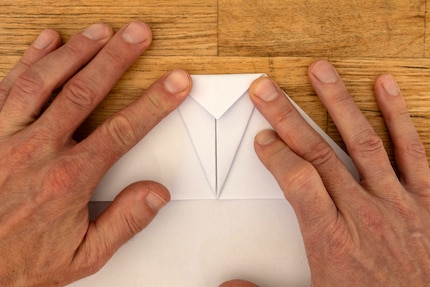 Sobald beide Seiten gefaltet sind, klappst du die Spitze des Fliegers nach hinten um.