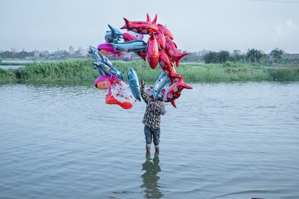 Ein Mann steht mit einem Bund Ballons im Wasser. Echte Fische gibt es in diesem Fluss nicht mehr.