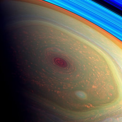 Der Nordpol von Saturn | Eine Kombination aus Bildern im sichtbaren Licht und im nahen Infraroten lässt in dieser Falschfarbendarstellung die Strukturen am Nordpol des Saturn besonders schön hervortreten. Exakt in der Bildmitte befindet sich der hier rötlich erscheinende Polarwirbel mit rund 2000 Kilometern Durchmesser. Ihn umgibt das polare Hexagon mit einem Durchmesser von etwa 20 000 Kilometern. Am rechten oberen Bildrand ist in Blau ein Teil der Saturnringe sichtbar.