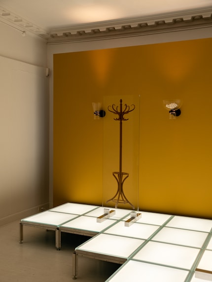 Against a mustard yellow background, the coat rack becomes a drawing on glass, flanked by two wall lamps.